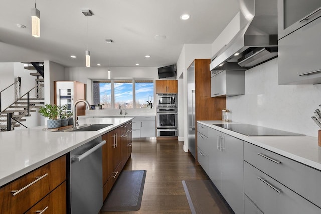 kitchen with modern cabinets, a sink, wall chimney range hood, stainless steel appliances, and light countertops