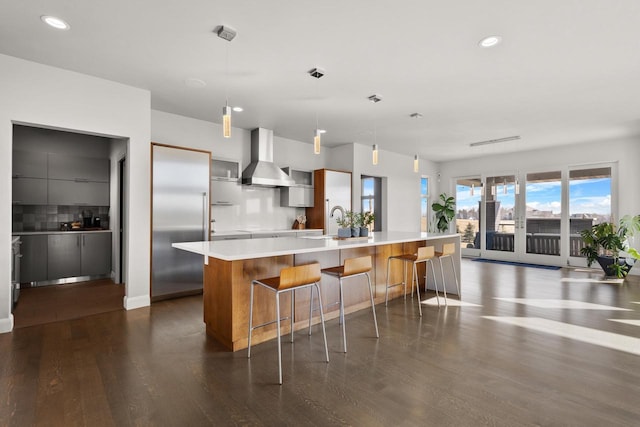 kitchen with backsplash, wall chimney range hood, built in refrigerator, light countertops, and modern cabinets