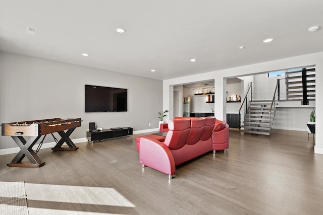 living area with wood finished floors, recessed lighting, a bar, baseboards, and stairs