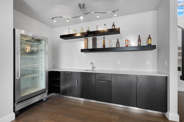 bar with indoor wet bar, dark wood finished floors, built in fridge, and a sink