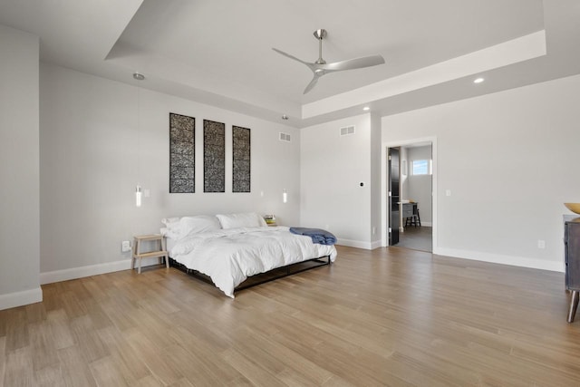 bedroom featuring a tray ceiling, baseboards, visible vents, and light wood-type flooring