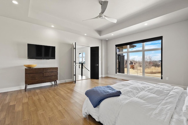 bedroom with a raised ceiling, recessed lighting, light wood-type flooring, and baseboards