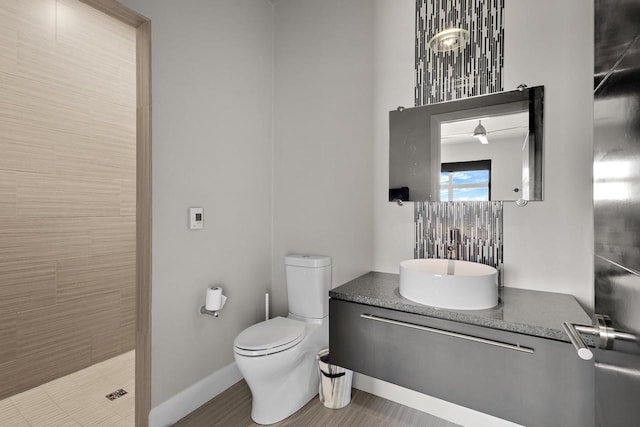 bathroom with baseboards, toilet, vanity, and a tile shower