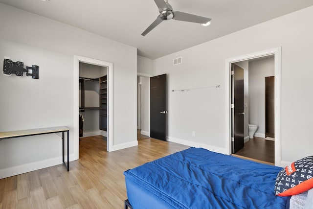 bedroom featuring visible vents, a walk in closet, baseboards, light wood-style flooring, and ensuite bathroom