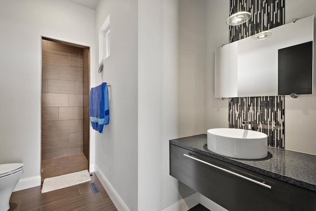 bathroom featuring baseboards, toilet, tiled shower, wood finished floors, and vanity