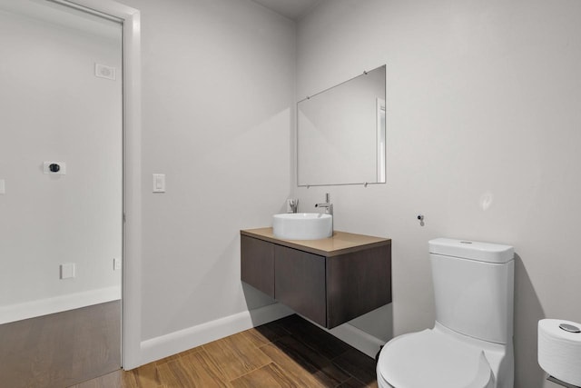 bathroom featuring toilet, vanity, baseboards, and wood finished floors