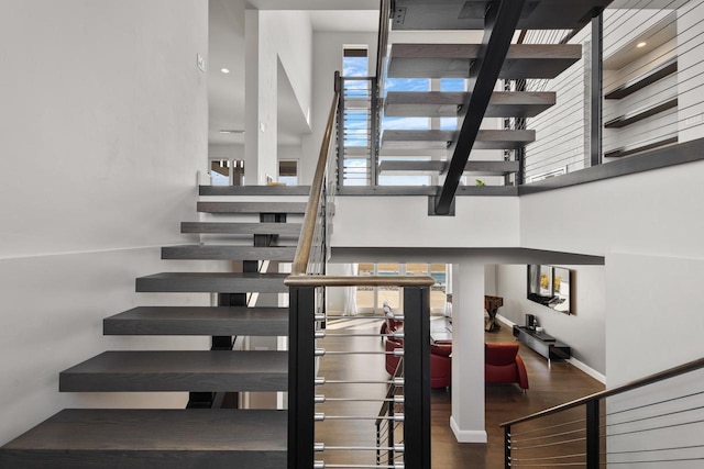 staircase with baseboards, wood finished floors, and a towering ceiling