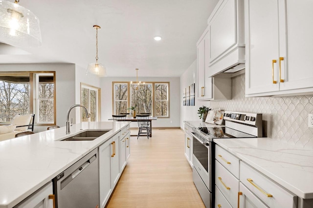 kitchen with a sink, appliances with stainless steel finishes, decorative light fixtures, tasteful backsplash, and light wood-type flooring