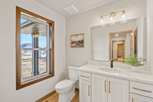 half bath with vanity, toilet, wood finished floors, and baseboards