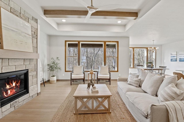 living area with beam ceiling, ceiling fan with notable chandelier, light wood-type flooring, and baseboards