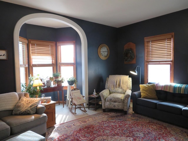 living area featuring arched walkways, plenty of natural light, and light colored carpet