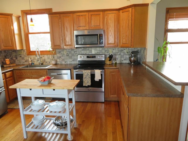 kitchen with light wood-style flooring, appliances with stainless steel finishes, a peninsula, and a sink