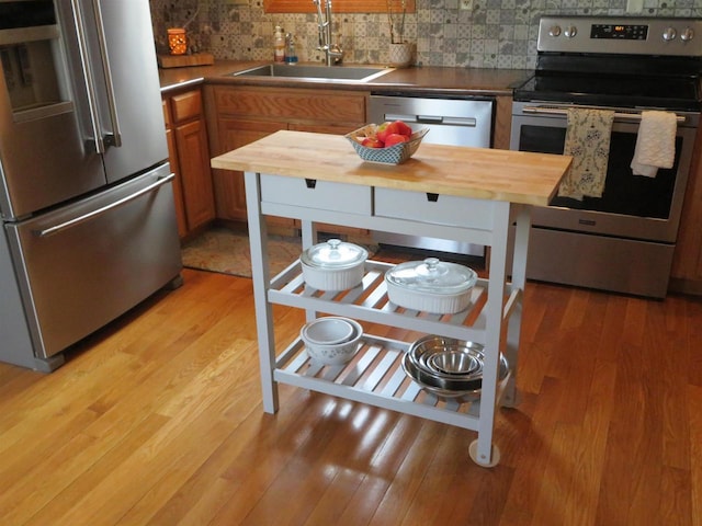 kitchen featuring light wood-type flooring, brown cabinets, a sink, tasteful backsplash, and appliances with stainless steel finishes