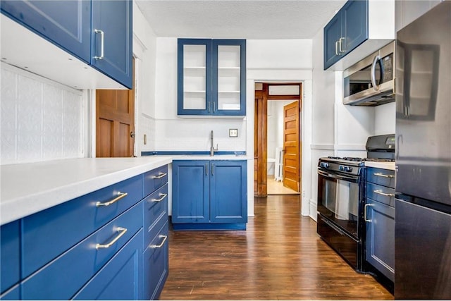 kitchen featuring blue cabinetry, dark wood-style flooring, stainless steel appliances, light countertops, and glass insert cabinets