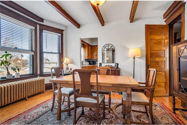 dining area featuring beamed ceiling, radiator, and light wood-style floors