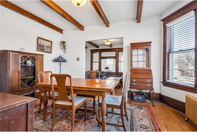 dining space featuring baseboards, beamed ceiling, wood-type flooring, and a healthy amount of sunlight