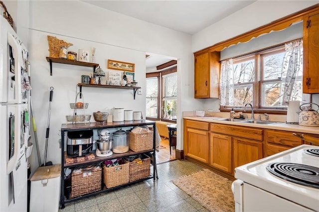 kitchen with a sink, light countertops, brown cabinetry, electric range, and open shelves