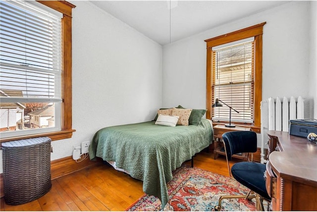 bedroom with multiple windows, wood-type flooring, and radiator heating unit