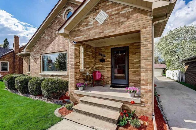 doorway to property featuring a yard, brick siding, and covered porch