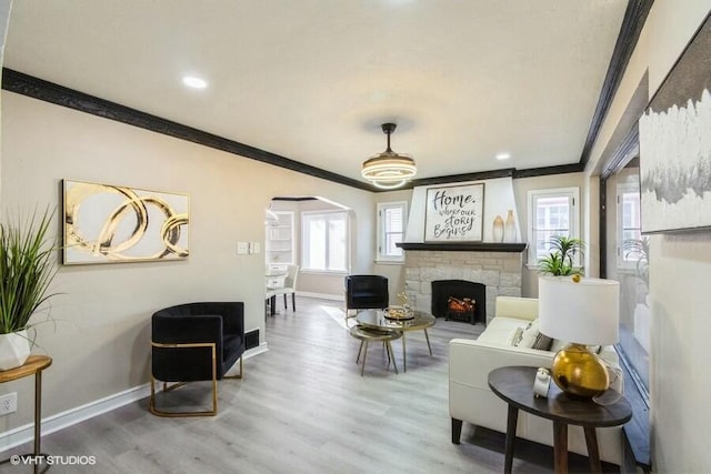 living room with crown molding, baseboards, a stone fireplace, wood finished floors, and arched walkways