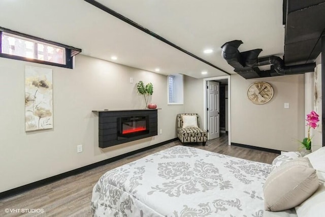 bedroom featuring a glass covered fireplace, baseboards, and wood finished floors