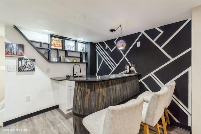 bar featuring wet bar, wood finished floors, baseboards, and a sink