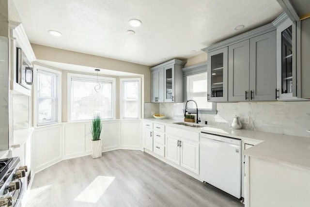 kitchen with gray cabinetry, a sink, high end stainless steel range oven, white dishwasher, and light countertops