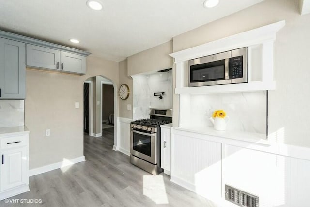 kitchen featuring visible vents, gray cabinets, light wood-style flooring, arched walkways, and stainless steel appliances