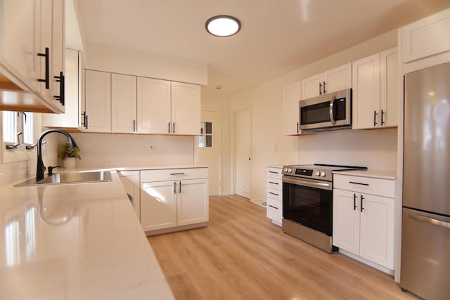 kitchen featuring light wood-type flooring, light countertops, stainless steel appliances, white cabinetry, and a sink