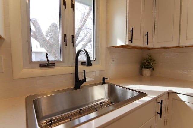 interior details featuring a sink, white cabinetry, tasteful backsplash, and light countertops