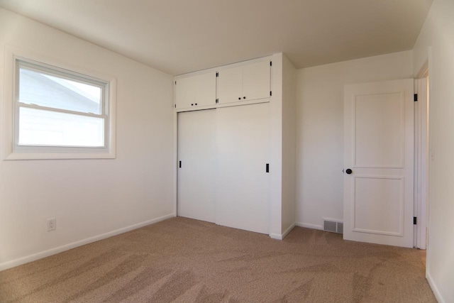 unfurnished bedroom featuring baseboards, visible vents, a closet, and light carpet