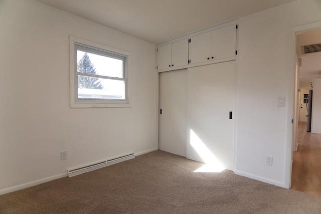 unfurnished bedroom with a baseboard heating unit, light colored carpet, visible vents, and a closet