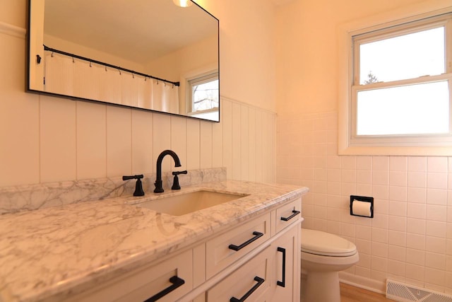 bathroom with vanity, visible vents, wainscoting, tile walls, and toilet