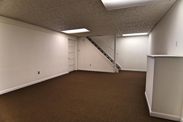 finished basement with dark carpet, stairs, baseboards, and a paneled ceiling