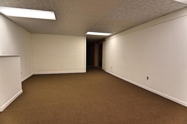 empty room featuring a paneled ceiling, baseboards, and dark colored carpet