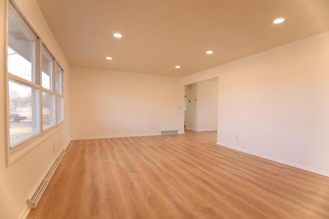 empty room featuring a baseboard heating unit, light wood-style flooring, recessed lighting, and visible vents