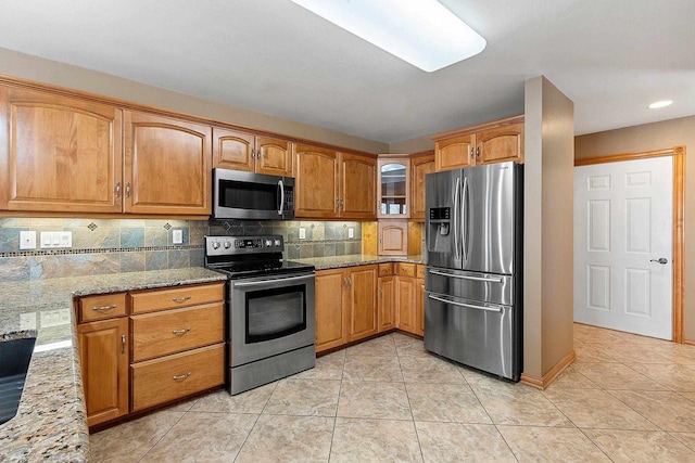 kitchen with stainless steel appliances, light stone countertops, brown cabinets, and decorative backsplash