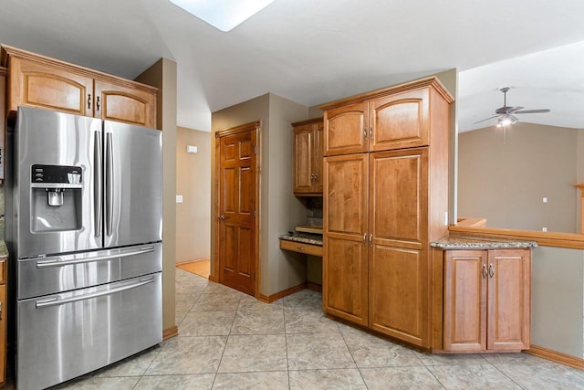 kitchen featuring ceiling fan, light stone countertops, lofted ceiling, brown cabinets, and stainless steel fridge