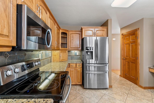 kitchen featuring backsplash, stainless steel appliances, baseboards, light tile patterned floors, and light stone countertops