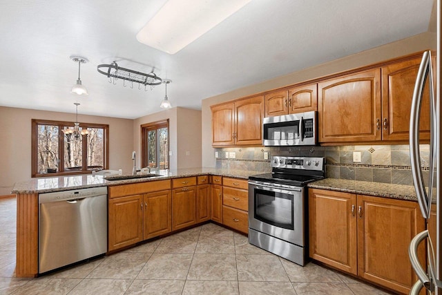 kitchen with a sink, light stone counters, backsplash, stainless steel appliances, and a peninsula