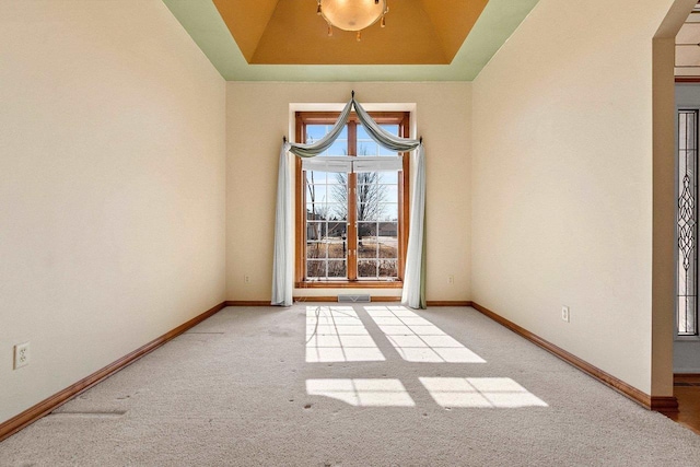 carpeted spare room with a raised ceiling and baseboards