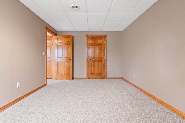 unfurnished bedroom with baseboards, visible vents, a drop ceiling, and light carpet