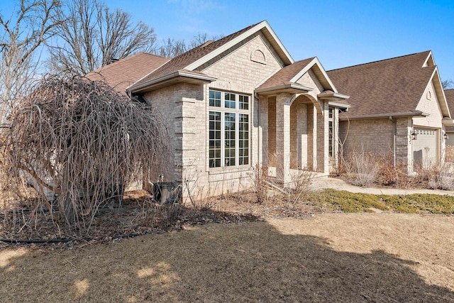 view of front of home with stone siding, an attached garage, brick siding, and roof with shingles