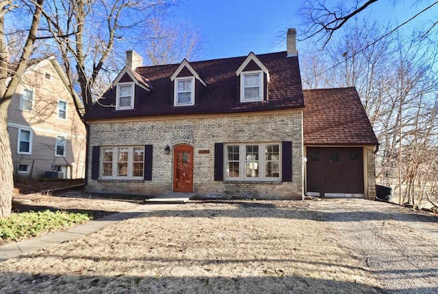 cape cod house featuring brick siding, cooling unit, an attached garage, and a chimney