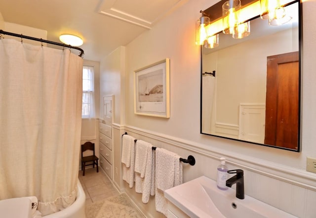 full bath with tile patterned flooring, a wainscoted wall, shower / tub combo with curtain, and a sink