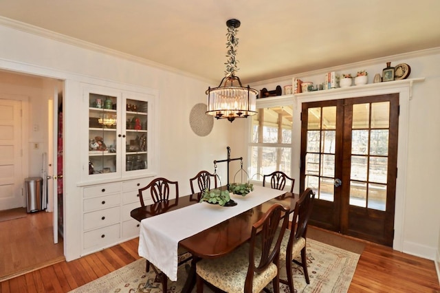 dining room with crown molding, french doors, light wood-type flooring, and a chandelier