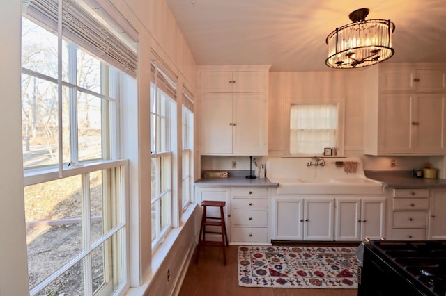 kitchen with wood finished floors, a sink, hanging light fixtures, white cabinetry, and a chandelier