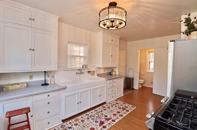 kitchen with appliances with stainless steel finishes, an inviting chandelier, wood finished floors, white cabinetry, and a sink