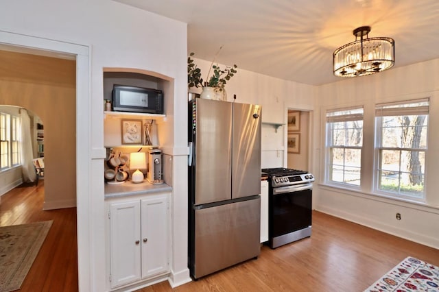 kitchen with light wood-type flooring, arched walkways, appliances with stainless steel finishes, and a chandelier