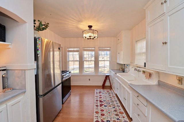 kitchen with light wood-style flooring, a sink, appliances with stainless steel finishes, white cabinets, and an inviting chandelier